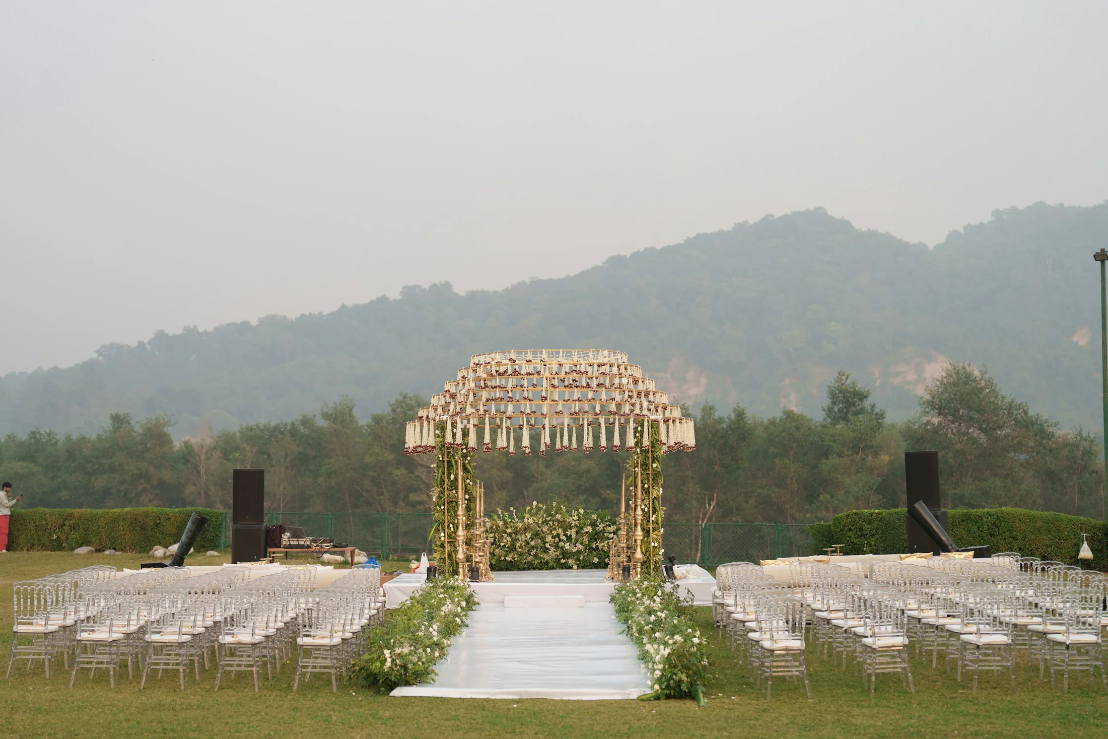 An Indian wedding ceremony setting with a jasmine-draped mandap, a white floral aisle, and rows of crystal chairs