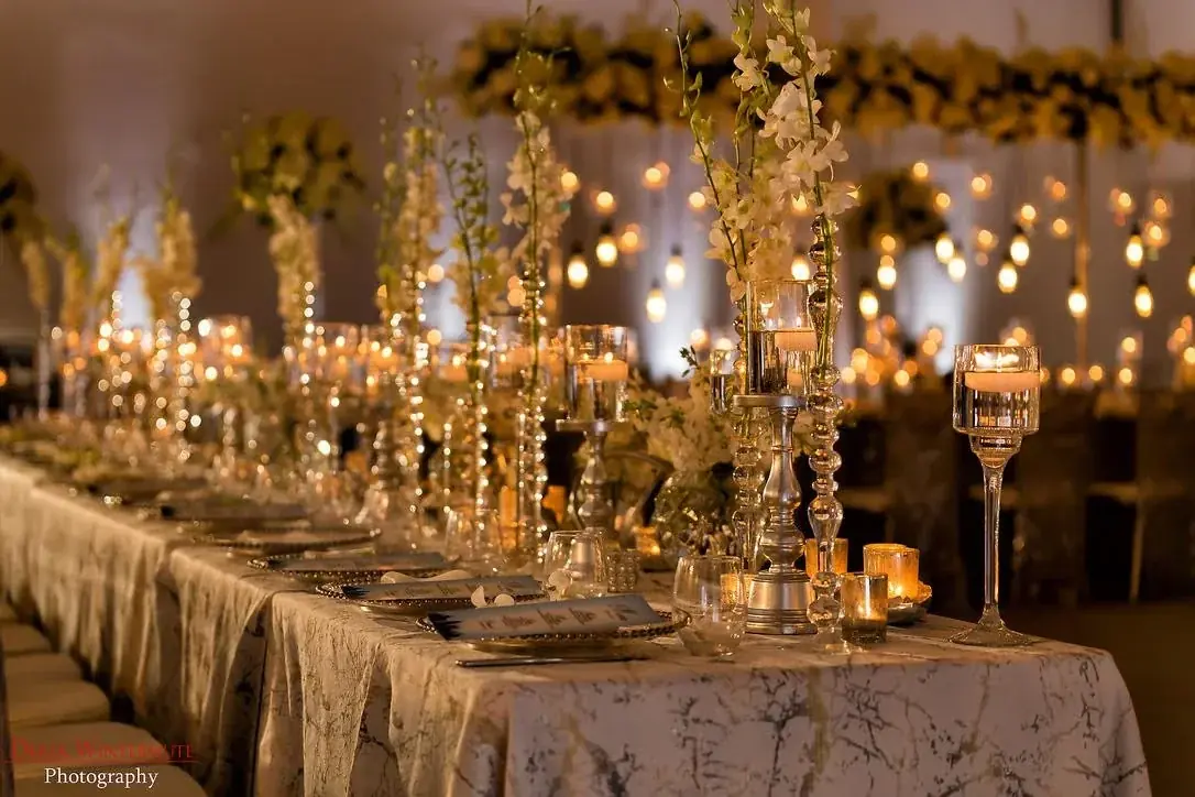A warm candlelit Indian wedding reception with ivory roses and glowing glass votives
